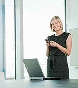 A smiling woman holding a phone with a laptop on a table